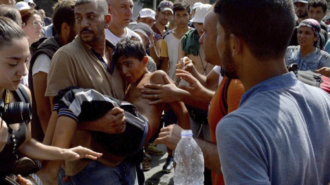 Refugiados llevan en brazos a un niño que se desmayó durante la larga espera para el procedimiento de registro en la isla griega de Lesbos. - EFE