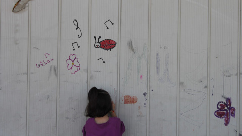 Una niña dibuja en una pared del campo de Sindos, en los alrededores de Tesalónica. - TOMÁS PARRA