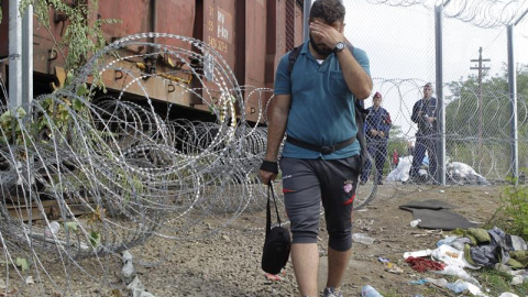 Un refugiado y dos agentes húngaros junto a la valla que separa Hungría de Serbia. - EFE