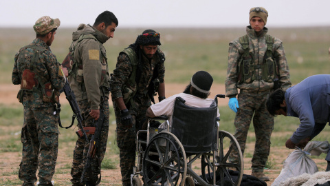 Combatientes de las Fuerzas Democráticas Sirias junto a un hombre en silla de ruedas en la ciudad de Baghouz. /REUTERS