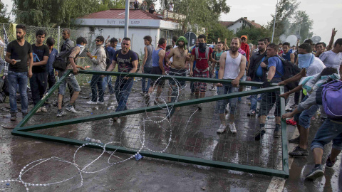 Un grupo de refugiados sostiene la puerta de la valla fronteriza con Hungría tras arrancarla. REUTERS