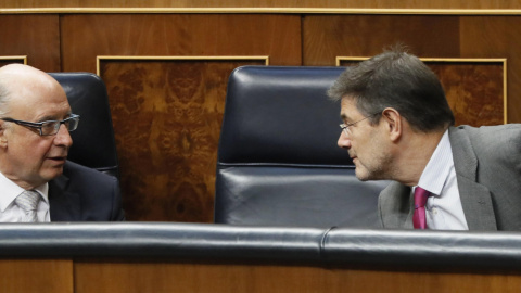 El ministro de Hacienda, Cristóbal Montero, conversa con el ministro de Justicia, Rafael Catalá, durante el Pleno del Congreso de los Diputados. EFE/ Fernando Alvarado