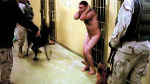 Un prisionero iraquí detenido por militares estadounidenses se encoge bajo de la amenaza de dos perros en la tristemente célebre prisión de Abu Ghraib. Las fotos de militares desvelaron los malos tratos y vejaciones a los detenidos en esa p