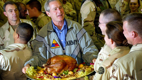 El expresidente de EEUU, George W. Bush, posa para una foto portando un pavo de Acción de Gracias durante su visita a las topas estadounidenses en Bagdad, el 27 de noviembre de 2003. El pavo resultó ser una recreación falsa de plástico.- TI