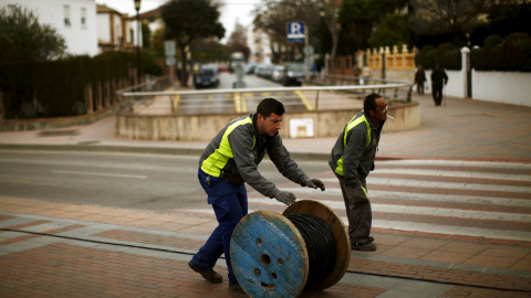 Dos trabajadores trasladan un rodillo de cable eléctrico en la localidad malagueña de Ronda. REUTERS / Jon Nazca