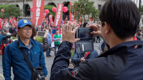 Unos turistas asiáticos se fotografían al paso de la manifestación del Primero de Mayo en Sevilla , donde miles de personas se han dado cita para reivindicar la igualdad de género, el empleo de calidad y las pensiones dignas, y cuyo lema es