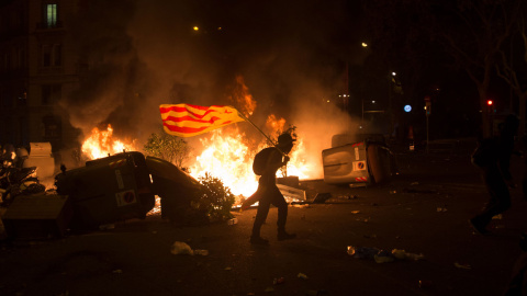 Un joven con una bandera estelada camina entre los contenedores en llamas en Barcelona. GUILLEM SANS