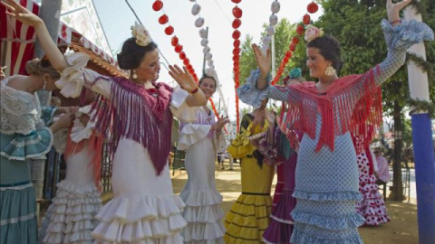 Jóvenes vestidas con el traje típico de flamenca bailan sevillanas en el Real de la Feria de Abril de la capital hispalense. EFE/Archivo