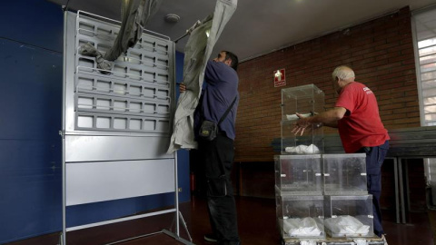 Dos operarios descargan varias urnas e instalan una cabina en un colegio electoral en Barcelona. EFE/Alberto Estévez