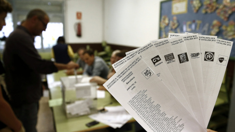 Una persona muestra las papeletas de los diferentes partidos que concurren a las elecciones al Parlament, mientras una persona deposita su voto en la urna. EFE/ Jesús Diges