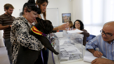 Una mujer carga con su perrro (que lleva en el collar los colores de la bandera catalana) frente a la urna de su colegio electoral en  Barcelona. REUTERS/ Gustau Nacarino