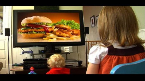 Niños viendo en la televisión un anuncio de comida poco saludable.