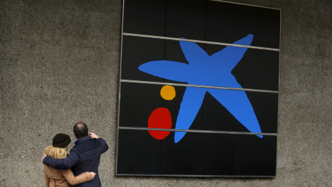 Una pareja se hace un selfie junto a una de las oficinas de Caixabank en Madrid. REUTERS