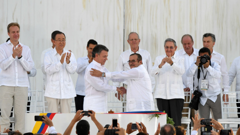 El presidente de Colombia, Juan Manuel Santos, estrecha la mano al máximo líder de las FARC, Rodrigo Londoño Echeverri, alias "Timochenko", tras firmar los Acuerdos de Paz. - AFP