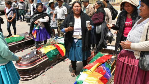 16/11/2019.- Un grupo de mujeres realiza una ceremonia ante los féretros de varios de los fallecidos tras los disturbios de ayer con las fuerzas del orden, frente al Instituto de Investigaciones Forenses este sábado, en Cochabamba (Bolivia)