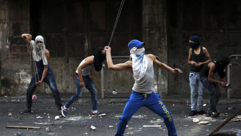 Varios palestinos lanzan piedras durante los enfrentamientos registrados con policías israelíes en la ciudad cisjordana de Hebrón.