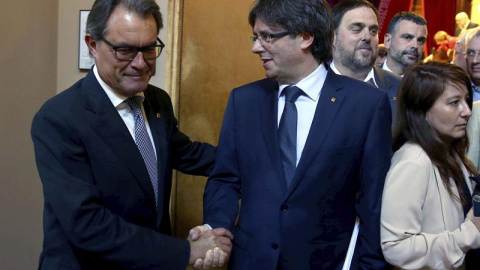 El presidente de la Generalitat, Carles Puigdemont, recibe el saludo del expresidente catalán, Artur Mas, tras su intervención en el debate de la cuestión de confianza, la primera que vive el Parlament desde que fue restablecido y para la q