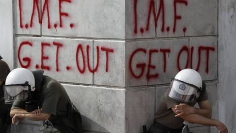 Un par de policías antidisturbios descansan junto a una pintada contra el FMI, durante una manifestación contra las medidas de austeridad (5 de mayo de 2010). REUTERS/Yorgos Karahalis