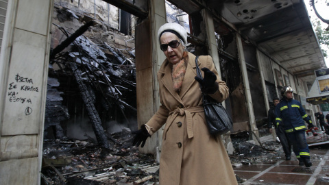 Una mujer pasa junto a un comercio quemado tras los incidentes ocurridos durante la noche que siguió a la aprobación del Parlamento griego de un paquete de medidas de ajuste (13 de febrero 2012). REUTERS / John Kolesidis