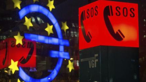 Fotografía que muestra el símbolo del Euro reflejado en una ventana junto al letrero luminoso de un teléfono de emergencia, en Fráncfort, Alemania. EFE