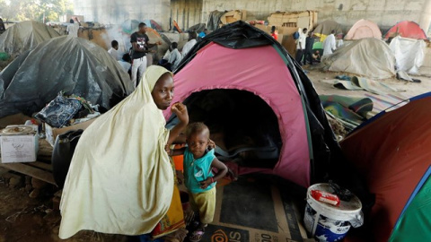 Una madre, junto a su hijo, en una acampada de personas migrantes. / Reuters