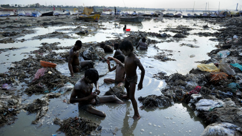 Varios hombres buscan oro y monedas en el agua contaminada del río Ganga, en Sangam. AFP