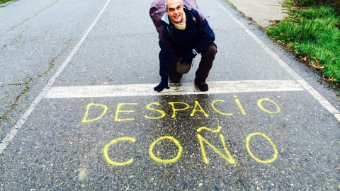 Susaeta posando en una carretera señalando una pintada en la que se lee 'Despacio coño'.