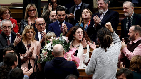 a diputada del grupo de Unidas Podemos Aina Vidal (c), que hoy ha asistido a votar a pesar de estar enferma de cáncer, recibe un ramo de flores de sus compañeros al término de la segunda y definitiva votación./ Mariscal (EFE)