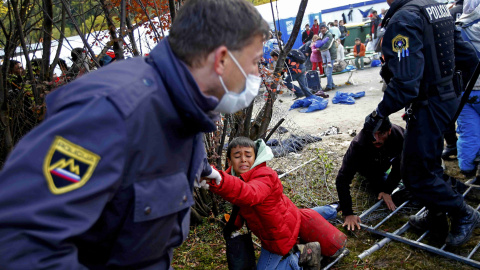 Un oficial de la policía eslovena levanta a un niño después de que una multitud de refugiados rompiera el cordón policial para escapar del campo de refugiados y llegas hasta Austria.- REUTERS / Leonhard Foeger