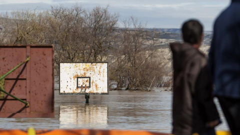 Varias personas observan un campo de baloncesto anegado por la crecida del río Ebro, hoy en la localidad de Cabañas de Ebro. Las motas de contención están aguantado el caudal del Ebro y la noche ha transcurrido en los pueblos de la ribera z