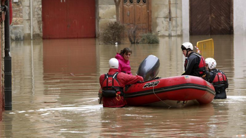 Voluntarios de Cruz Roja acompañan a una mujer hasta su casa por las calles anegadas del casco histórico de Tudela (Navarra), dentro de la atención que prestan a los vecinos que han quedado incomunicados por la crecida del río Ebro, desbord