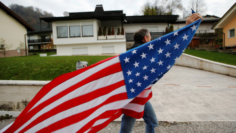 Un hombre ondea una bandera de Estados Unidos delante de la casa de los padres de Melania Trump. / SRDJAN ZIVULOVIC