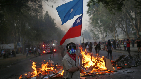 Un manifestante sostiene la bandera de Chile frente a una barricada en llamas en Santiago, Chile. REUTERS / Edgard Garrido