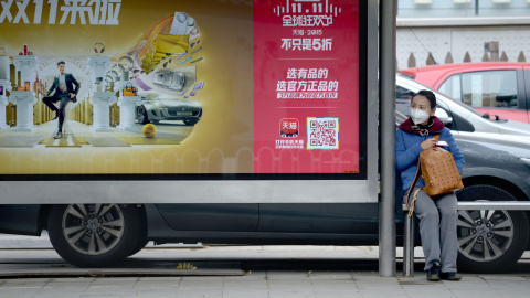 Una mujer espera al autobús junto a un anuncio publicitario del "Single Day". AFP PHOTO / WANG ZHAO