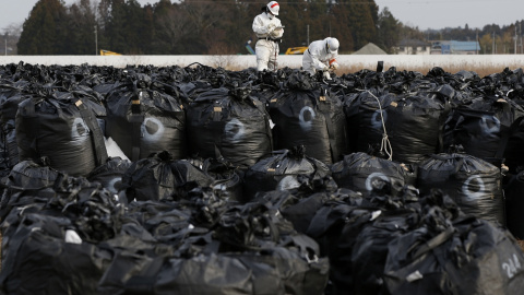 Trabajadores con trajes protectores y máscaras transportan grandes bolsas de plástico con tierra contamianda, hojas y desechos, en las tareas de descontaminación de Tomokia, cerca de TEPCO./ REUTERS-Toru Hanai