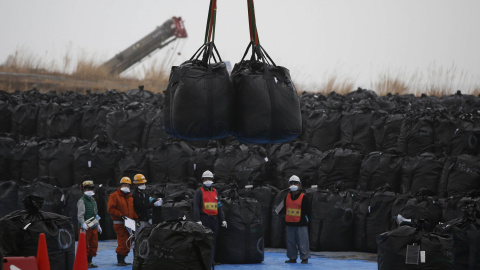 Trabajadores mueven grandes bolsas de plástico que contienen desechos contaminados en un depósito temporal, dentro de la operación de descontaminación de la zona, en la ciudad de Tomioka, provincia de Fukushima./ REUTERS-Toru Hanai