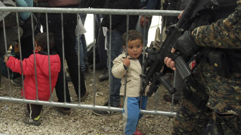 Un niño refugiado contempla el arma de un militar serbio, mientras espera para ser registrados en el campo de refugiados de Presevo, al sur de Serbia. EFE/Djordje Savic