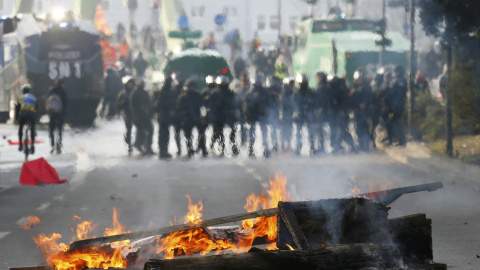 Un contenedor quemado en Fráncfort y de fondo una hilera de antidisturbios. /REUTERS