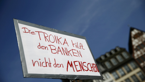 Una pancarta que dice, en alemán, "La Troika ayuda a los bancos y no a las personas", durante la concentración contra la austeridad en la UE celebrada en la plaza del Ayuntamiento, en el centro histórico de Fráncfort, tras la inauguración d