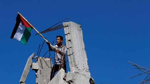 Un hombre sostiene una bandera palestina sobre las ruidas de una de las casas destruidas por los bombardeos de Israel en la Franja de Gaza. REUTERS/Mohammed Salem