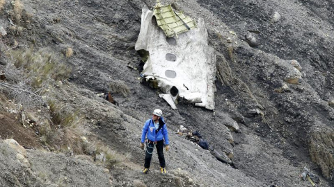 Un miembro de los servicios de rescate camina al lado del mayor un tramo de fuselaje del avión siniestrado, en el que se aprecian tres ventanillas, entre millones de fragmentos del aparato esparcidos por una amplia área de alta montaña en l