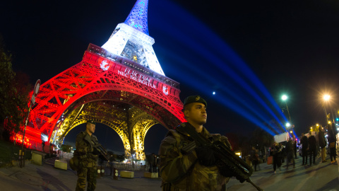 Un soldado francés monta guardia tras declararse una alerta de seguridad en Francia, frente a la Torre Eiffel,iluminada con los colores de la bandera francesa en homenaje a las víctimas de los atentados de París.-  AFP PHOTO / JOEL SAGET