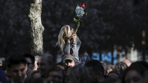 Una niña sostiene un ramo de flores sobre los hombros de sus padre durante un homenaje a las víctimas de los ataques de París en el National Memorial del 11-S de Manhattan, Nueva York.- REUTERS / Andrew Kelly