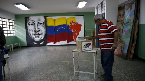 Un ciudadano venezolano deposita su voto con un mural de Chavez al fondo, en Caracas. REUTERS/Carlos Garcia Rawlins