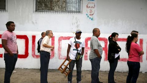 Un grupo de votantes espera su turno ante un graffiti de Hugo Chavez donde se lee "Paz. Vive". REUTERS/Nacho Doce