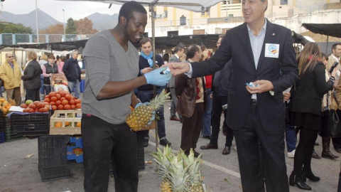 El presidente del grupo parlamentario del PP de Catalunya, Xavier Garcia Albiol, entrega un mantecado con propaganda electoral del PP a uno de los vendedores durante la visita que ha realizado hoy al mercadillo de las Albarizas de Marbella,