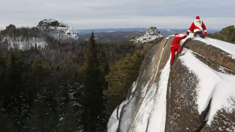 Un miembro de 'Sibspas', grupo de búsqueda y rescate siberiano, vestido de Papá Noel, le a la mano a su compañero que está disfrazado del Padre Invierno, mientras escalan la roca del 'Cuarto Pilar' en la Reserva Nacional de la Naturaleza de