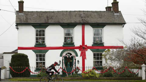 Un hombre montado en una bicicleta pasa por una casa decorada con regalos de Navidad. Norte de Bretaña. REUTERS/Phil Noble