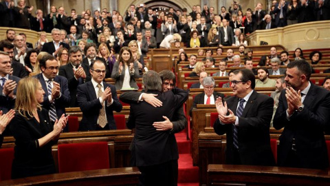 El presidente catalán en funciones, Artur Mas (de espaldas), saluda a Carles Puigdemont, poco antes de comenzar el pleno del Parlament en el que se debate la investidura de Puigdemont como nuevo presidente de la Generalitat, tras el pacto a