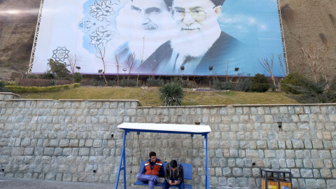 Dos jóvenes iraníes se sientan bajo una gran foto del fallecido líder de Irán, el ayatolá Jomeini, y el líder supremo de Irán, el ayatolá Ali Jamenei en un parque de Teherán, Irán. REUTERS